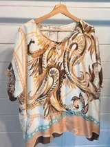 Blusa de satén con estampado de cadenas y hojas en tonos blanco, marrón y negro. Tiene corte amplio, mangas cortas y cuello redondo. Se ajusta a la cintura con un cinturón elástico negro con hebilla dorada.