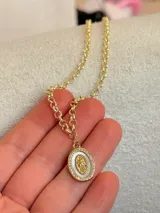 Collar de cadena de eslabones redondos con baño de oro, con dije ovalado que presenta una figura central en relieve, fondo de nácar y borde pavé con circonias.
