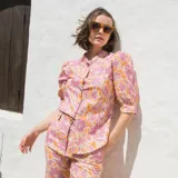 Camisa de lino con estampado floral en tonos rosados y naranjas, de corte recto, cuello mao y cierre frontal con botones. Presenta mangas al codo con frunces en los hombros.