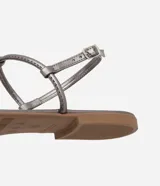 Sandalia plana color dorado, con diseño de tiras finas y aplicación de pedrería decorativa en la parte central. Cuenta con cierre de hebilla lateral ajustable.