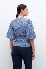 Blusa cruzada celeste con estampado floral, mangas cortas abullonadas y lazo en la cintura.