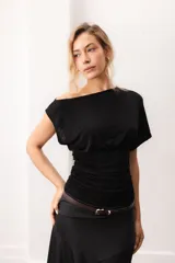 Top negro de manga corta ancha y escote bote con caída asimétrica en los hombros. Presenta un diseño ajustado en la cintura con frunces laterales.