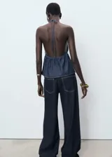Top de denim con escote halter, espalda abierta y diseño evasé. Cuenta con fruncido elástico y cierre de lazo en el escote delantero.
