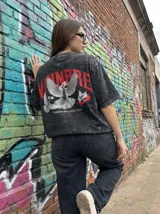 Remera negra con efecto lavado, corte oversize y estampado de palomas y texto en rojo.