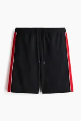 Short de ripstop negro con corte holgado, cintura elástica con cordón de ajuste y franjas laterales rojas con ribete blanco.