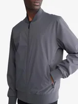 Campera bomber Calvin Klein color gris, confeccionada en poliéster resistente al agua con acabado mate. Cuenta con cuello redondo, cierre frontal completo, bolsillos laterales con cierre, logo en el pecho y ribete de punto acanalado.