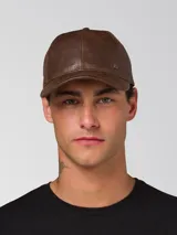 Gorro tipo gorra de béisbol con visera curva, confeccionado en cuero sintético con acabado texturizado. Presenta un pequeño aplique metálico con el logo de la marca en el lateral frontal y cierre metálico ajustable en la parte posterior.