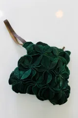 Cartera de mano verde oscuro hecha de círculos de lana merino afieltrada teñida artesanalmente, con asa de cuero marrón.