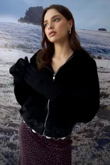 Chaqueta tipo teddy color negro, con capucha, cierre frontal metálico y puños tejidos.