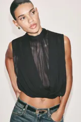 Blusa sin mangas blanca con estampado de lunares negros, cuello alto drapeado y nudo frontal en el bajo.