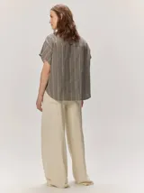 Camisa de manga corta color beige con sutil diseño a rayas verticales, cuello camisero con detalle de botones decorativos en la solapa y cierre frontal oculto.