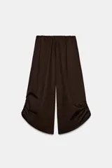 Pantalón culotte de tiro medio, color verde militar, con cintura elástica y bolsillos laterales ocultos. Presenta un diseño de bajo ancho con aberturas ajustables mediante cordones fruncidos en los laterales.