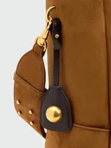 Bolso tipo cubo de gamuza en color marrón, con asa de hombro ajustable y detalle de dije metálico colgante.
