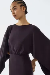 Vestido corto de punto fino en color negro, con escote bote, costura fruncida en la cintura y mangas capa largas con diseño abultado.