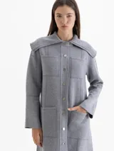 Tapado de tejido de punto color gris, con cuello tipo solapa grande, cierre frontal con botones a presión y bolsillos frontales. Presenta costuras decorativas visibles y diseño de largo medio.
