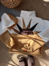Buzo de corderito con diseño de atardecer en la espalda, combinando colores blanco y camel. Presenta cuello alto con cierre y mangas largas.