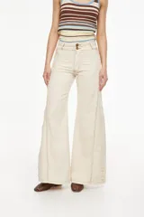 Pantalón jean beige de pierna ancha, con pretina doble y detalles de cortes laterales con flecos que recorren los laterales desde la cintura hasta el ruedo.