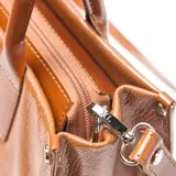 Cartera tipo tote de cuero texturizado color suela, con doble asa de mano y correa larga ajustable y extraíble. Presenta el logo de la marca grabado en el centro y cierre superior.