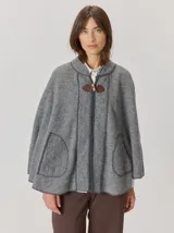 Capa de tejido de punto en color gris melange, con diseño abierto y cierre frontal mediante un botón tipo duffle de madera con detalle en cuero. Presenta bolsillos laterales amplios y bordes con costuras a la vista.