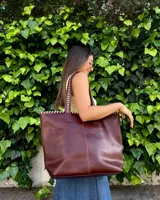 Bolso grande de cuero marrón, tipo shopper, con costuras artesanales decorativas en contraste a lo largo del borde superior y las asas de hombro.
