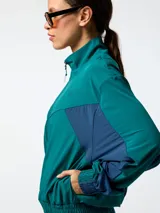 Campera cortaviento de microfibra oversize verde con inserciones azul marino en los costados y mangas, cuello alto y cierre frontal con cremallera.