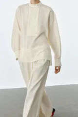 Camisa de manga larga confeccionada en seda 100%, con cuello mao y cierre frontal con botones. Presenta un diseño con bajo asimétrico y puños clásicos.