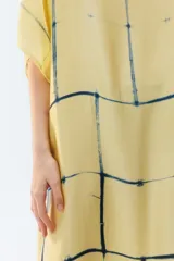Kaftan maxi amplio de color amarillo, con escote redondo, mangas cortas y ruedo irregular. Presenta un diseño estampado a cuadros con efecto teñido.