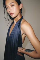 Mono largo satinado de color azul marino, con cuello halter, escote en V profundo y espalda descubierta. Presenta diseño plisado y bajo abullonado con terminación en puño.