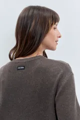 Cardigan negro de punto con acabado brillante, cuello redondo, cierre frontal de botones y detalle de cordones laterales entrelazados. Presenta mangas tres cuartos con diseño acampanado.