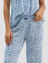 Pijama compuesto por remera sin mangas con escote redondo, botones frontales y detalle de puntilla, acompañado de un pantalón capri con cintura elástica. Presenta un estampado floral en tonos rosados sobre base gris.
