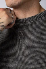 Buzo de corte oversize confeccionado en tela waffle de algodón con proceso de teñido acid wash. Presenta cuello redondo con detalle de costura en X y mangas largas con puños acanalados.