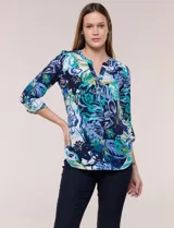 Blusa de gasa estampada de la marca Zac & Rachel, con diseño floral en tonos azul, celeste y verde sobre base blanca. Presenta escote en V con abertura y botones frontales, y mangas largas de largo regulable con presilla.