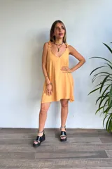 Vestido corto color amarillo mostaza, con escote en V y tirantes finos con detalle de volado o fruncido. El ruedo es asimétrico.