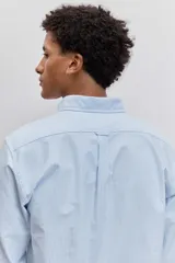 Camisa de manga larga en color celeste con estampado de rayas verticales finas, cuello abotonado y cierre frontal con botones.