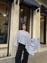 Poncho de hilo liviano en color gris, con diseño sin cuello y caída fluida. Presenta un corte asimétrico y una textura tejida, ideal para superponer sobre otras prendas.