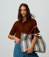 Cartera shopper de algodón con diseño a rayas en tonos neutros y detalles de ribetes y asas de hombro en PU marrón. Cuenta con una abertura central pronunciada y gran capacidad de almacenamiento.