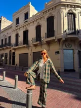 Blazer de corte recto con estampado de cuadros en tonos verdes, beige y negro, con cierre frontal de botones y bolsillos laterales.
