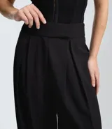 Pantalón de sastrería corte barrel, color marrón oscuro, con pliegues delanteros, cintura con cierre desplazado y piernas anchas.
