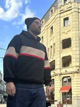 Canguro negro con capucha y cordones ajustables, con bloque horizontal color beige y línea roja.