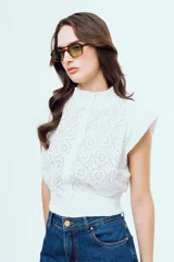 Top blanco sin mangas de broderie, con cuello alto, hombreras y cierre frontal de botones.