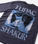 Remera de corte relajado color gris oscuro, con cuello redondo y manga corta. Presenta una estampa frontal pequeña en color blanco con el logo de Tupac.