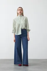 Camisa de viscosa con estampado de lunares, cuello alto con volados y cierre frontal de botones. Presenta un diseño de silueta suelta con frunces que aportan volumen y mangas largas con puños ajustados.