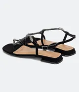 Sandalia baja Satinato, tipo chatita, de color negro con tiras adornadas con pedrería brillante y un detalle metálico en forma de serpiente. Cuenta con cierre de hebilla ajustable en el tobillo.