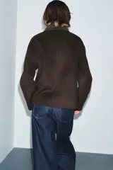 Chaqueta de corte recto confeccionada en hilatura con lana, en color marrón oscuro. Presenta cuello clásico en tejido efecto piel de ante, cierre frontal con cremallera metálica y manga larga.