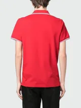 Remera polo Moncler confeccionada en piqué de algodón color rojo, con cuello y puños acanalados con líneas blancas y detalle de parche con logo en el pecho.