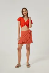 Minifalda color terracota de diseño cruzado, con lazo lateral para atar y volados en el borde delantero y en el ruedo.
