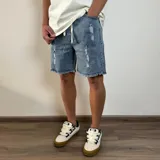 Bermuda tipo jogger de jean azul con efecto lavado, detalles de roturas y ruedo desflecado. Cuenta con cintura elástica con cordón ajustable.