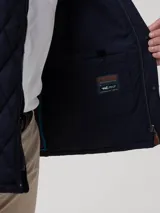 Campera acolchada azul marino con costuras en rombos, cuello de pana negro y cierre frontal con botones a presión. Incluye bolsillos laterales con ribete de pana y broches ajustables en la cintura.