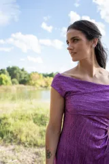 Vestido midi color violeta con textura brillante, escote off-shoulder y mangas cortas.