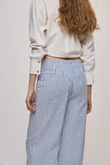 Pantalón de pierna ancha y tiro medio con diseño de rayas verticales blancas y azules. Cuenta con bolsillos delanteros amplios y cierre frontal con botón y cremallera.